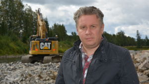 Vägbyggmästare Niklas Brandt. En man som står vid en å bredvid en grävmaskin.