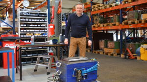 Tom Ståhlberg visar formen de använder för att tillverka plastlådor. Man i blå tröja och beiga byxor står bakom en fabriksform och framför varuhyllor i en fabriksbyggnad.