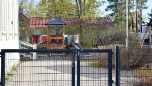 Den här grinden till daghemmet Petters gård är stängd, men inte låst. Föräldrar med barn i daghemmet vill definitivt inte att grinden eller dörrarna ska bommas igen för gott. Gården på ett daghem. En stängd järngrind och inne på gården ser man en rutsckana och en klätterställning som liknar ett hus.