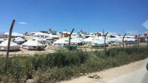 Internationella organisationer och Syriska Röda halvmånen är några av de som finansierar lägret, ihop med Syrian Democratic Forces myndigheter. Bakom ett stängsel kan man se en vit tältby i ett ökenlandskap.