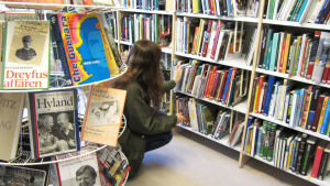 Man kan inte leta böcker i hyllorna. De böcker man vill låna bör beställas och avhämtas. En kvinna står på huk framför en bokhylla i biblioteket och letar efter böcker