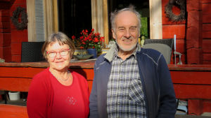 Beatrice och Dallas Hammarberg har bott på flera håll i Finland. Före Bromarv bodde de i Kervo, men båda ville flytta tillbaka till sina gamla hemknutar. De bor nu nära Beatrice gamla hemställe. Dallas kommer från Nitlax, men där håller barnen till. En äldre kvinna och äldre man står framför en rödmålad stockstuga. De ser in i kameran och ler.