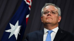 Morrison säger att Australien inte kommer att göra Kina till viljes. Istället planerar man att ta upp vissa av exportkonflikterna med Världshandelsorganisationen WTO, med hänvisning till att Kina bryter mot WTO:s regler. Scott Morrison on mustan kankaan edessä. Hänellä on tumma puku ja vaaleansininen kravatti. Taustalla näkyy Australian lippu.