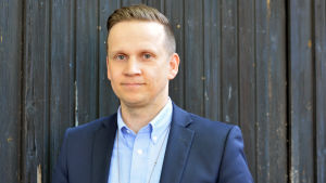 Förundersökningsledare Mats Sjöholm vid Raseborgspolisen säger att polisen kan göra en utredning utan att prata med anhöriga. Ibland krävs det till och med lov för att informera anhöriga. Personporträtt av kriminalkommissarie Mats Sjöholm. Han står vid en mörk dörr i klädd en mörkblå kostym.