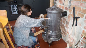 Om det blir svalt inne får man elda lite mer i ugnen konstaterar Saara. Hunden Nelson ser på när hon sätter ved i sin kamin. bild på en kvinna och hennes hund
