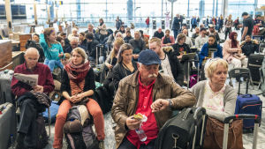 Över hundratusen resenärer har drabbats av flygstrejken. De här resenärerna väntar på besked på Gardermoen i Oslo. Resenärer sitter och väntar på en flygplats och en man tittar på klockan.