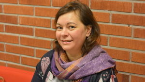Karin Ljung-Hägert är invandrarkoordinator i Raseborg. En kvinna som ser in i kameran. Röd tegelvägg i bakgrunden.