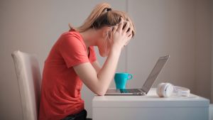 Arbetsrum hemma är avdraget framom andra för distansjobbaren i beskattningen 2020. Kvinna i röd t-shirt sitter vid ett bord med uppfälld laptop och lutar huvudet i händerna
