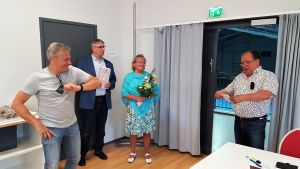 Leif Ström (längst till vänster) fick gåvor och tack av kommundirektör Juha-Pekka Isotupa, kommunstyrelsens ordförande Merja Laaksonen och fullmäktiges ordförande Heikki Kaisla. Tre glada män och en kvinna med en blombukett står i ett kontorsrum. Mannen till vänster gör en coronahälsning med armbågen.