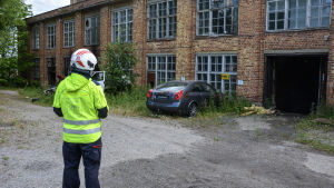 Ryggen av person i räddningsverkets kläder som betraktar gammal byggnad som brunnit.