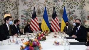 USA:s utrikesminister Antony Blinken och Ukrainas utrikesminister Dmytro Kuleba Mnisterit ja muut virkamiehet istuvat pitkän valkoisella pöytäliinalla peitetyn pöydän vasremmalla ja oikealla puolella. Miehillä on tummat puvut ja maskit. Seinän vieressä on molempien maiden liput.