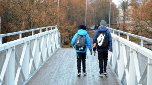 Gångbron över Hoplaksvägen i Helsingfors gör skolvägen säkrare för en del barn. Två pojkar på en bro.