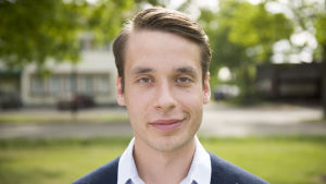 Henrik lägger runt 20 timmar i veckan på sitt arbete som ordförande. En man iklädd en ljusblå skjorta och en mörkblå tröja. Han är utomhus. I bakgrunden skymtar kommunhuset i Ingå.