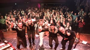 Gruppbild med finsk publik efter en lyckad spelning. Gruppen Fatboy poserar framför publiken på rockklubben Tavastia.