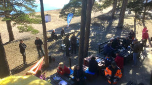 Mötet om och på Tullstranden samlade ett fyrtiotal intresserade plus ett halvt dussin experter och myndigheter. Människor på en uteservering på en sandstrand. Vår, solen skiner, havet är blått, folk sitter vid bord eller står och pratar i små grupper. Tallar växer på stranden.