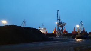 Snart är de här stenkolshögarna i Ingå hamn ett minne blott. En hög med stenkol och båt och kranar i bakgrunden.