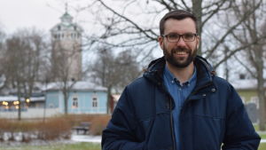 Johan Kvarnström hemma i Ekenäs på jullov. I januari ska Kvarnström bland annat delta i Nordiska Rådets möte i Köpenhamn, något han ser fram emot. En mörkhårig man med skägg o glasögon står i en park. Kyrka i bakgrunden. (Ekenäs)