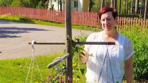 Anna Hjelm hemma på gården i Broby i Pyttis. Anna står i blomstrande trädgård i starkt solljus med väg och staket i bakgrunden.
