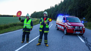 Kungsvägen stängdes av efter olyckan. Två män i neonvästar och stoppskyldar i händerna står på en väg och har en röd paketbil bakom sig. Kungsvägen stängdes av efter olyckan.