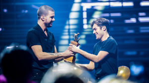 Fjolårsvinnaren Robin Bengtsson överräcker segertrofén till Benjamin Ingrosso En man ger en trofe till en annan man