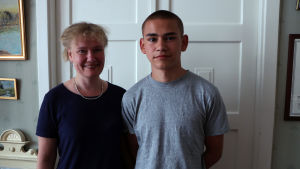 Kia och Alexander Brummer. En kvinna och en ung man står framför en vit dörr och ser in i kameran.
