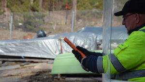 En man i gul reflexjacka och svart keps är beredd att skjuta iväg en nödraket. Han skyddar sig bakom en plexiglasskiva så att bara händerna och raketen kommer fram genom två hål i skivan.