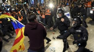 Upploppet utanför huvudpolisstationen började efter lördagens stordemonstration. Poliser med batonger angriper en demonstrant som bär på Kataloniens flagga