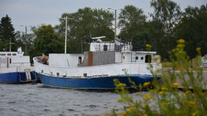 Suukko 2 ligger just nu förtöjd vid Räfsö utanför Björneborg. Båten är en gammal sovjetisk trålare, som paret hittade i Borgå skärgård. En blåvit, medelstor båt ligger vid en kaj.