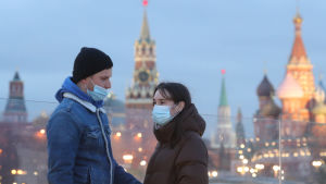 I Moskva sker undervisningen i många universitet på distans och från och med veckoslutet måste barer och restauranger stänga tidigare. En man och en kvinna med munskydd. Mannen har dragit ner sitt skydd så att näsan inte är täckt. Personerna står framför Vasilijkatedralen som är ett känt landmärke i Moskva.