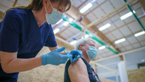 En man får Astra Zeneca-vaccin i Lojo i februari. Flera länder har nyligen pausat vaccinationerna med det svensk-brittiska vaccinet, efter misstankar om att det kan orsaka blodproppar. En man blir stucken med en spruta innehållande coronavaccin, av en sköterska i mörkblå kläder och ljusblå gummihandskar.
