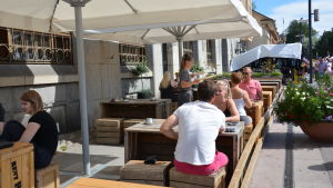 Fredrika Wulff har på sig en t-skjorta och ett par mörka byxor i sommarvärmen. Det är också okej att ha shorts eller kjol så länge knäna är övertäckta, berättar hon. servitris fredrika vid pub niska bär ut två pizzor i sommarvärmen