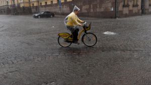 Översvämmade gator på Senatstorget. En cyklist cyklar genom ett kraftigt regn på Senatstorget i Helsingfors.