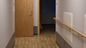 Korridorerna är smalare än på det nuvarande boendet. En korridor med ljust golv och dörrar på vardera sida.