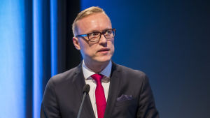Stadsdirektören ser tågleden som en del av hela östra Finlands utveckling, inte bara regionens. Man i mörk kostym talar vid ett podium.