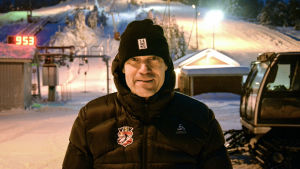 Mikael Nylund Medelålders man i svart vinterjacka och mössa tittar in i kameran och ler. I bakgrunden syns en slalombacke och en pistmaskin.