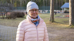 Tanja Koivisto har också oroligt följt med hur årskullarna i Hangö blir mindre. Alla ungdomar väljer inte heller att studera vidare i stadens gymnasier och på sikt kan skolorna vara hotade, säger hon. En kvinna med mössa och rosa, tunn vinterjacka står ute. Bakom tennisbana och klubbhus.