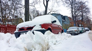 Autoja kadun varressa lumikinoksen alla.