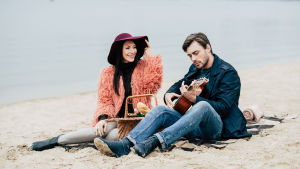 En picknick på stranden gör susen! Men bara om hon har på sig sin Muppet show-jacka och han sjunger Eagles-låtar och gör sin svåra min. Kvinna och man sitter på en sandstrand, han spelar gitarr