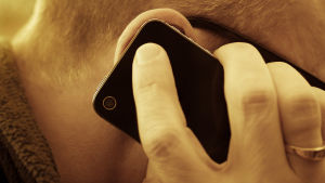 En närbild på en man som talar i en mobiltelefon. Mobilen och mannens hand täcker hans öra.
