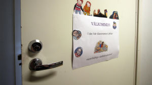I det här klassrummet går undervisningen på svenska. En klassrumsdörr med en lapp där det står "Välkommen - i det ähr klassrummet jobbar superhäftiga språkdetektiver."