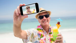 Hej - ifall ni missat så är jag på lyx-semester! #fyrkfinns #gillasnällaminbild #lifeisgreat äldre man med solhatt tar en selfie på stranden, har en drink i handen.