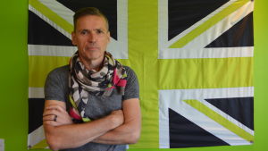 Dale Vince vill rädda världen. En man med allvarlig min står med armarna i kors framför en brittisk flagga där de fält som normalt är röda har ersätts med grön färg.