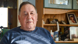 Henry Sandholm minns tiden då han jobbade med att leta efter uran. Efter arbetet på Käldö åkte han runt i Nyland och undersökte berggrunden, först tillsammans med en arbetskamrat i bil och därefter ensam på motorcykel efter att bilen gått sönder. En äldre man i blå tröja sitter i en stol i sitt vardagsrum. Han tittar in i kameran och ler.