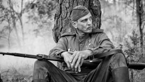 En fara eller ett beskydd? Barry Pepper spelar en av de människor som den lilla pojken möter. En soldat sitter under ett stort träd med begävert vilande på knäna.