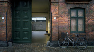 European Spermbank är inhyst i ett vanligt tegelhus på en mindre gata på Nørrebro. Tegelbyggnad med grön port och en cykel parkerad intill väggen.