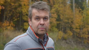 Håkan Lindgren efterlyser statistik på hur många långtradare som får grönt ljus vid polisens razzior. en man i grå-orange kläder ser in i kameran. Bakom höstgula och -röda lövträd.