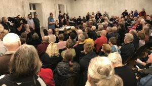 Invånarmöte med en fullsatt sal med mänskor som lyssnar på en talare längst fram.
