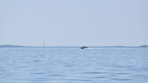 För många kan det vara skönt att slippa använda bottenfärg. En motorbåt på ett lugnt, klarblått hav en sommardag. Segelbåtar långt i fjärran.
