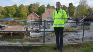 Vesa Noutia har lett arbetet med fiskvägen i den historiska bruksmiljön i Billnäs. Man i gul arbetsjacka står framför fiskväg i bruksmiljö.