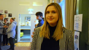 Nelli Salonen har bara jobbat som producent för ÅTS i någon vecka, men har redan hunnit med mycket. en kvinna i svartvitrutig kostym står bland andra människor i ett rum inomhus